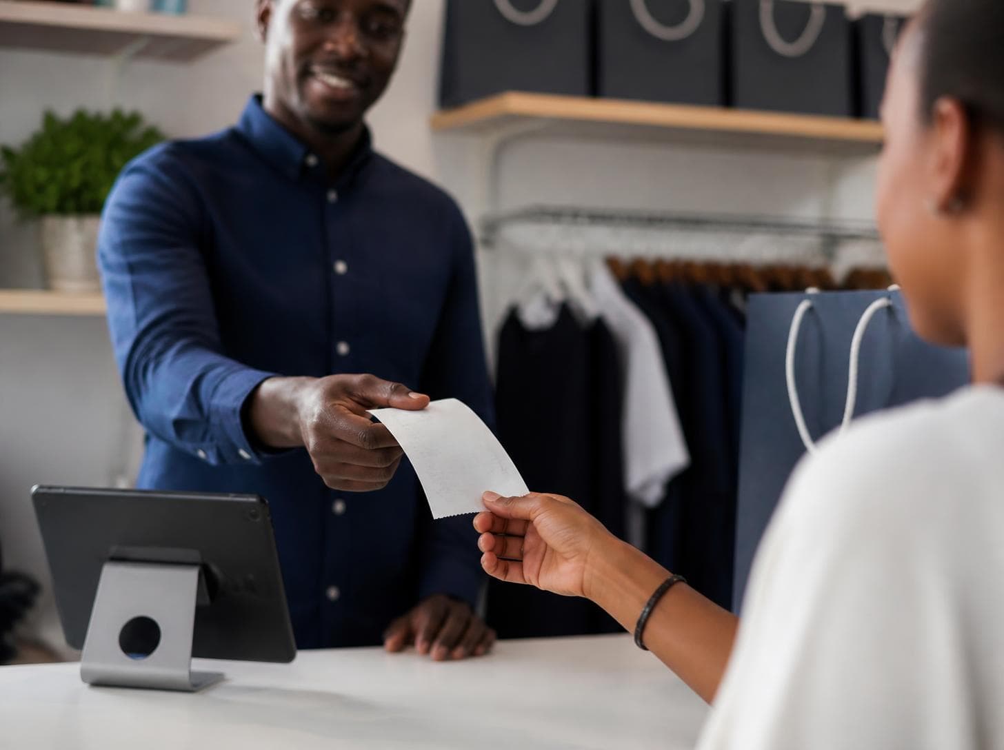 A shop owner handing over a receipt beside a point-of-sale tablet